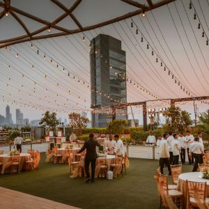 Elegant rooftop event with tables and lights set against Mumbai skyline at sunset, India.